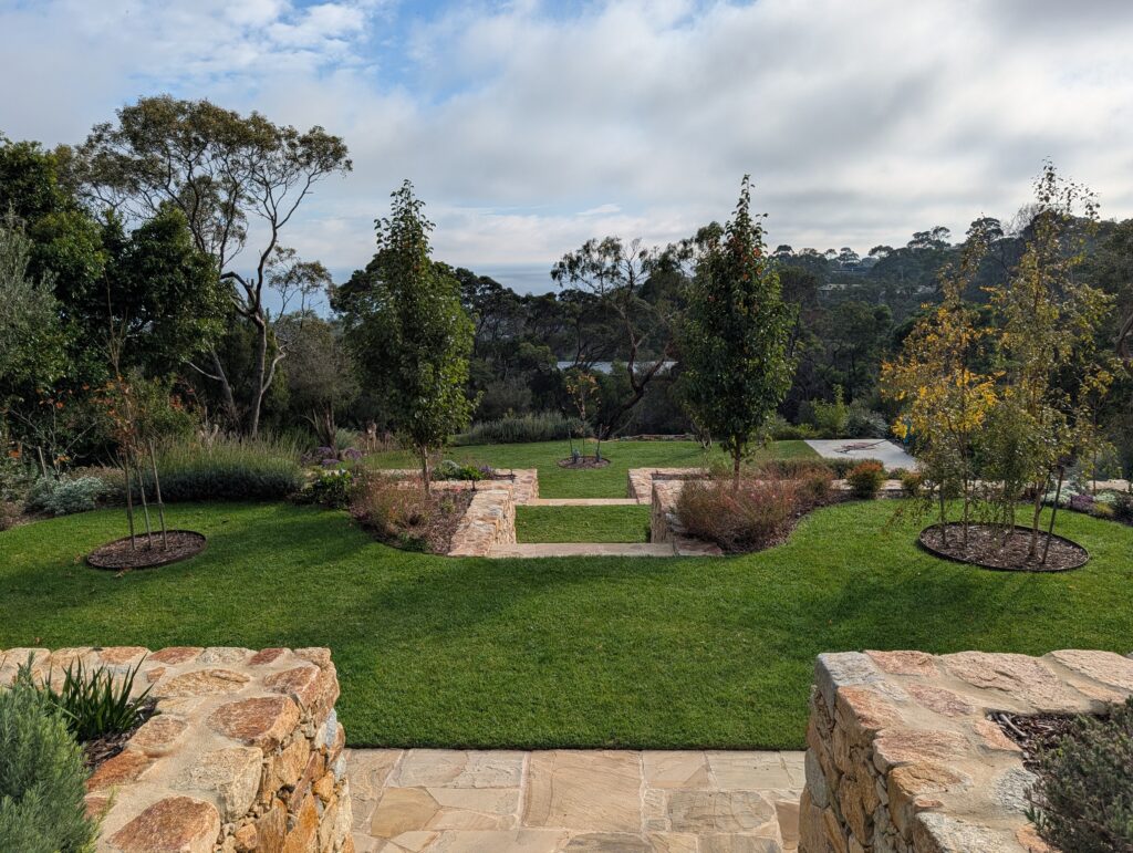 Terraced garden levels retained with dry stone walls. Indian sandstone stairs  leading to lawn areas, garden beds and trees.